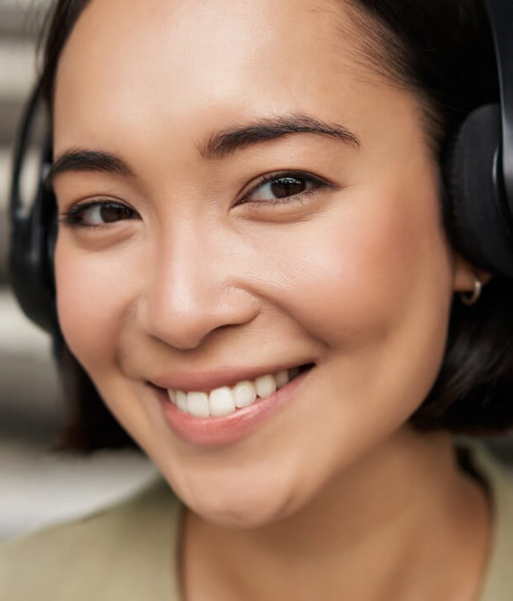 close-up-portrait-smiling-asian-girl-headphones-listens-music-outdoors-looking-happy